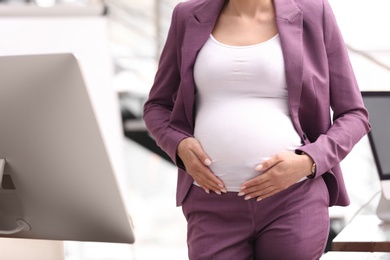 Young pregnant woman in suit at workplace, closeup