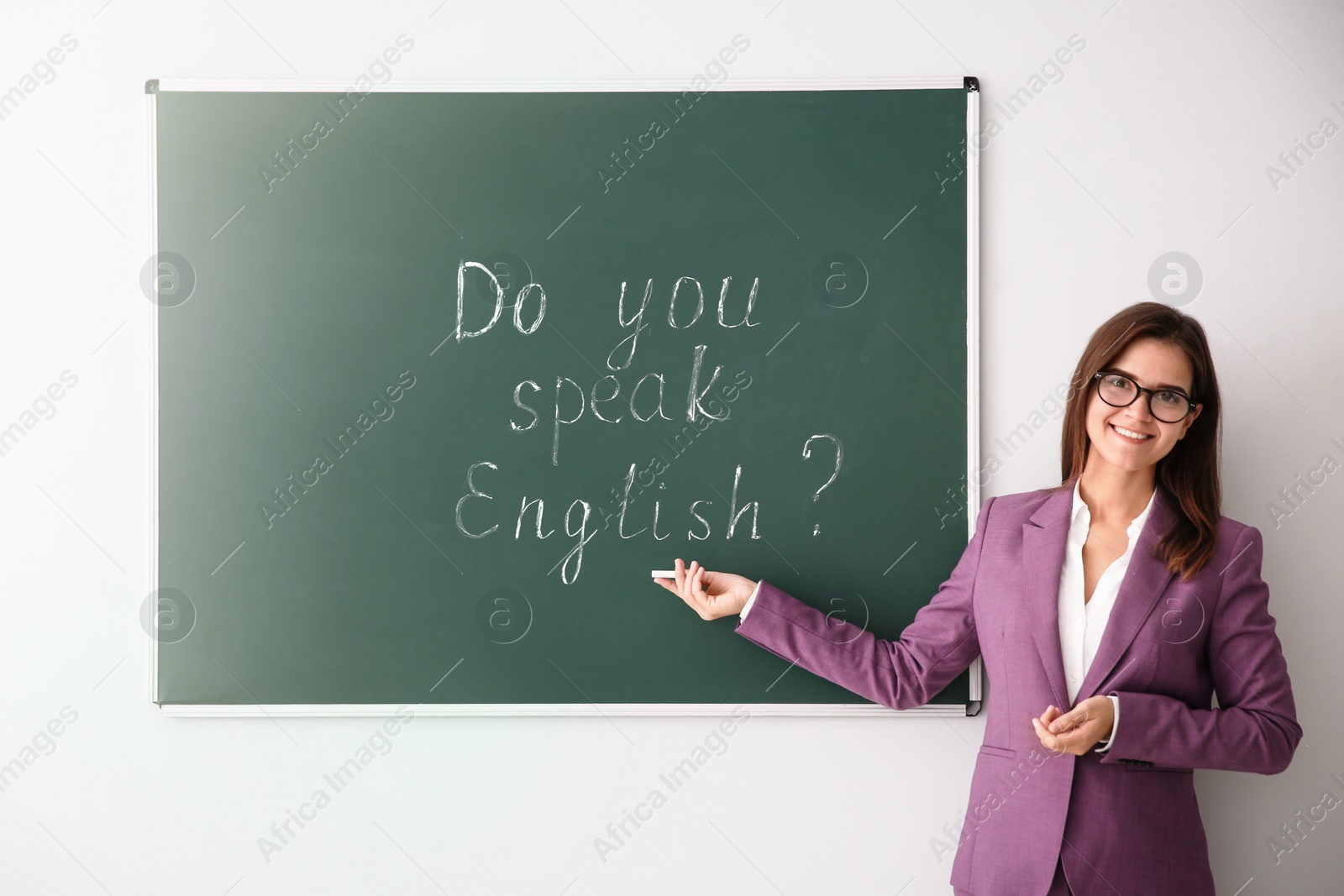 Photo of Teacher near green chalkboard with words Do You Speak English?