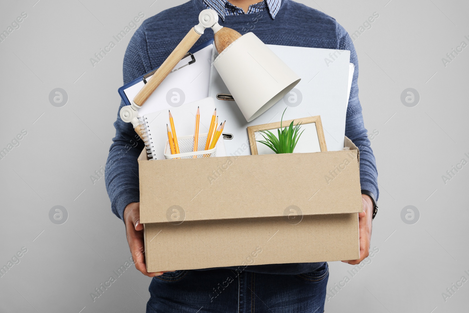 Photo of Unemployed man with box of personal office belongings on light grey background, closeup