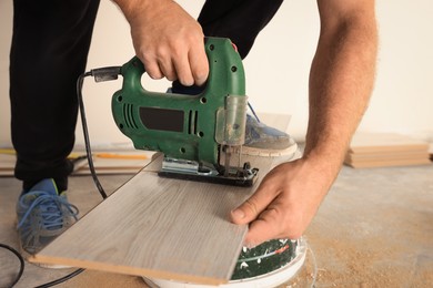 Photo of Professional worker using jigsaw during installationnew laminate flooring, closeup