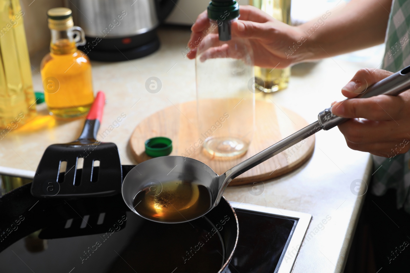 Photo of Woman with used cooking oil and empty bottle near stove in kitchen, closeup