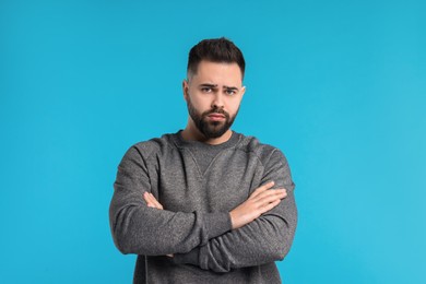 Photo of Portrait of sad man with crossed arms on light blue background