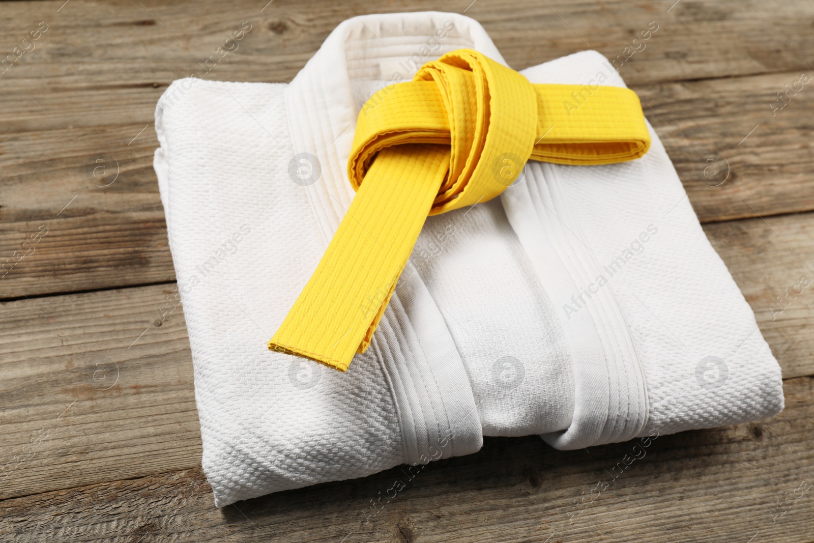 Photo of Yellow karate belt and white kimono on wooden background