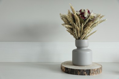 Beautiful bouquet of dry flowers on white table near light wall, space for text