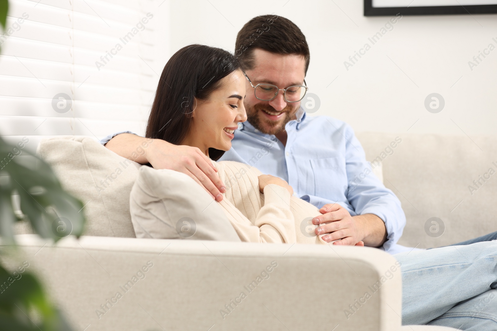 Photo of Happy pregnant woman spending time with her husband on sofa at home