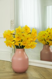 Photo of Beautiful daffodils in vase on floor indoors, space for text