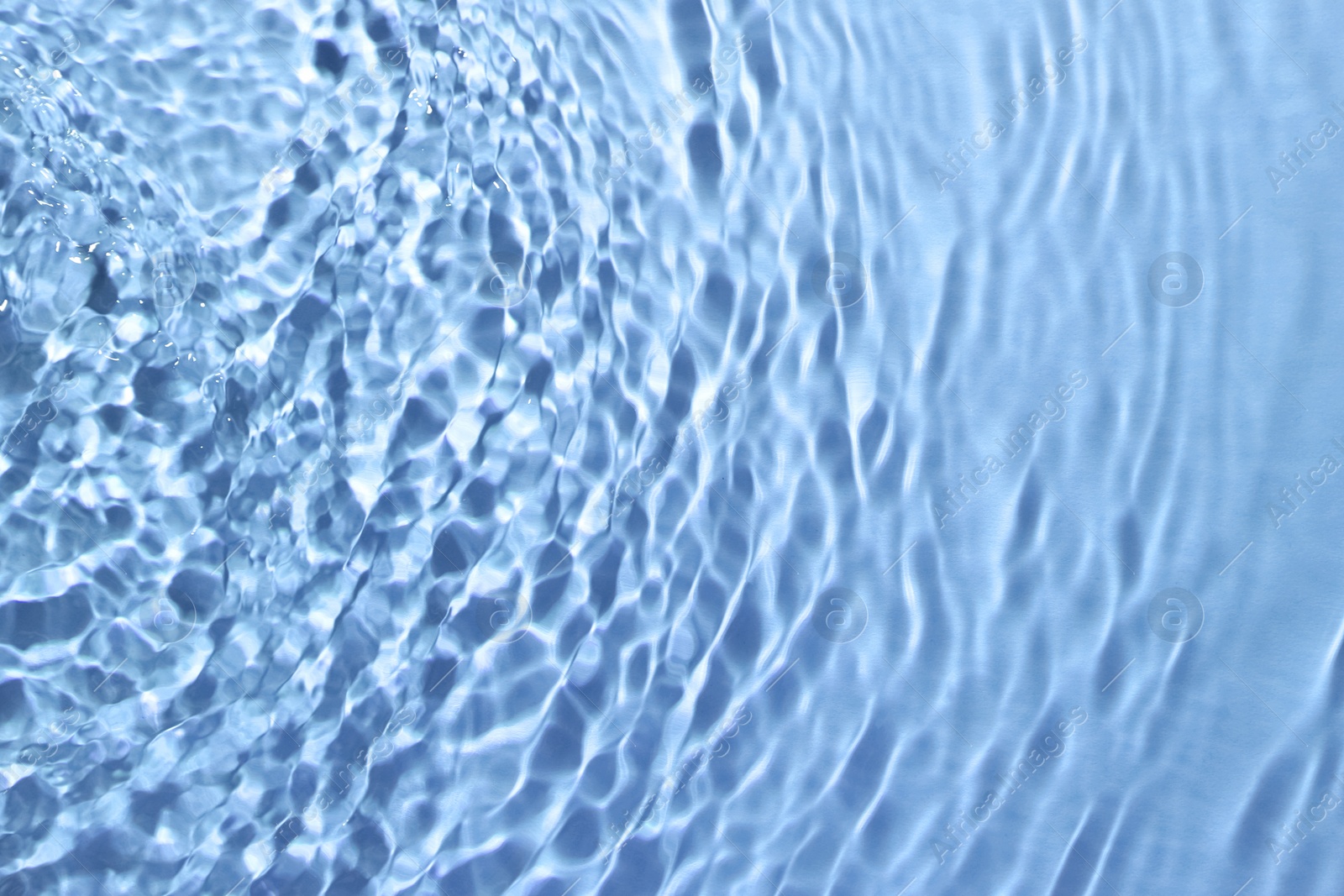 Image of Rippled surface of clear water on light blue background, closeup