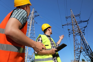 Photo of Professional electricians in uniforms near high voltage towers