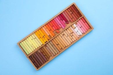 Photo of Set of soft pastels in wooden box on light blue background, top view. Drawing material