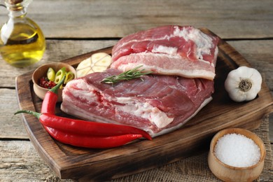 Photo of Pieces of raw pork belly, chili peppers, oil, garlic and rosemary on wooden table