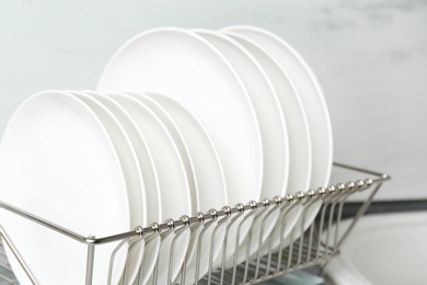 Photo of Different clean plates in dish drying rack on kitchen counter