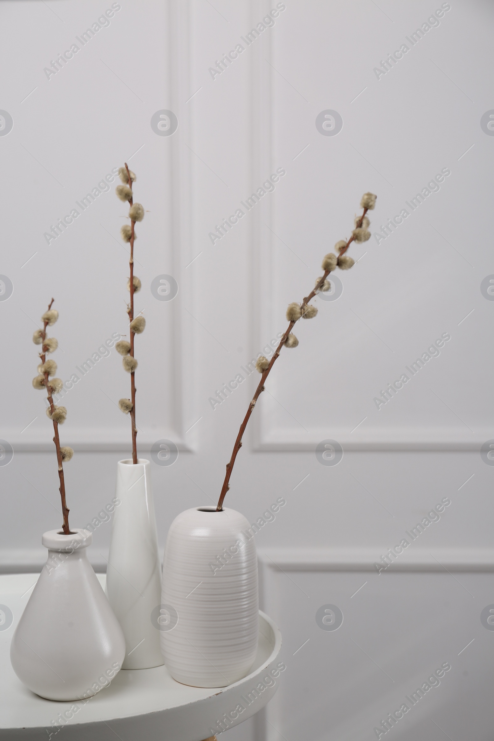 Photo of Beautiful pussy willow branches in vases on white table indoors