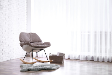 Photo of Comfortable rocking chair, rug and basket near white brick wall. Space for text