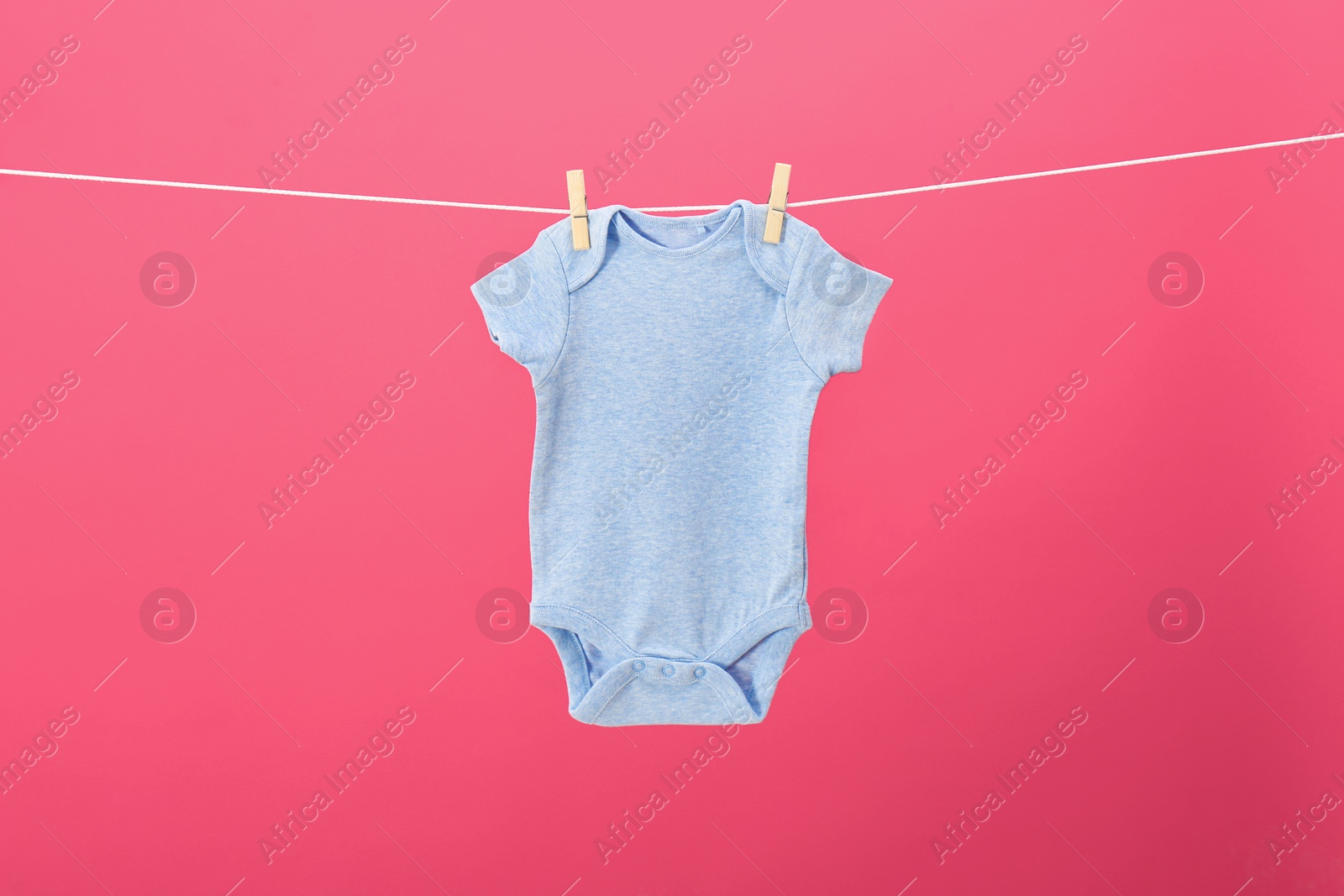 Photo of Baby onesie hanging on clothes line against pink background