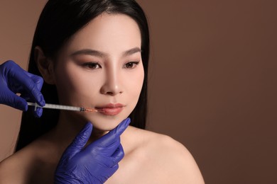 Photo of Woman getting lip injection on brown background