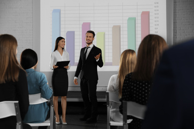 Photo of Business trainers giving lecture in conference room with projection screen