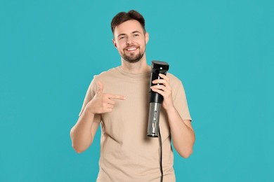 Smiling man pointing on sous vide cooker against light blue background