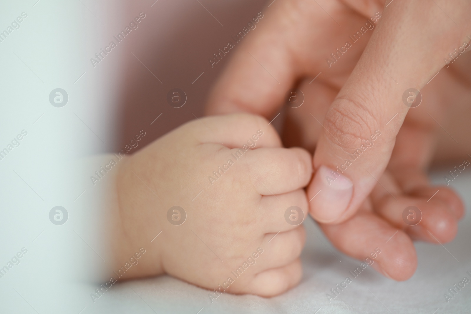 Photo of Baby holding motherʼs hand on bed, closeup