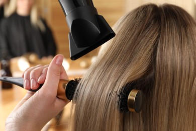 Photo of Hairdresser blow drying client's hair in salon, closeup