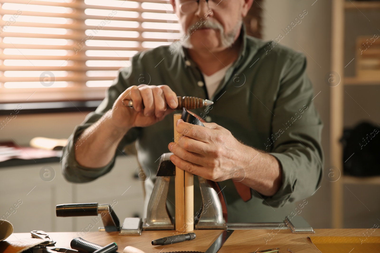 Photo of Man burnishing edges of leather belt in workshop, closeup