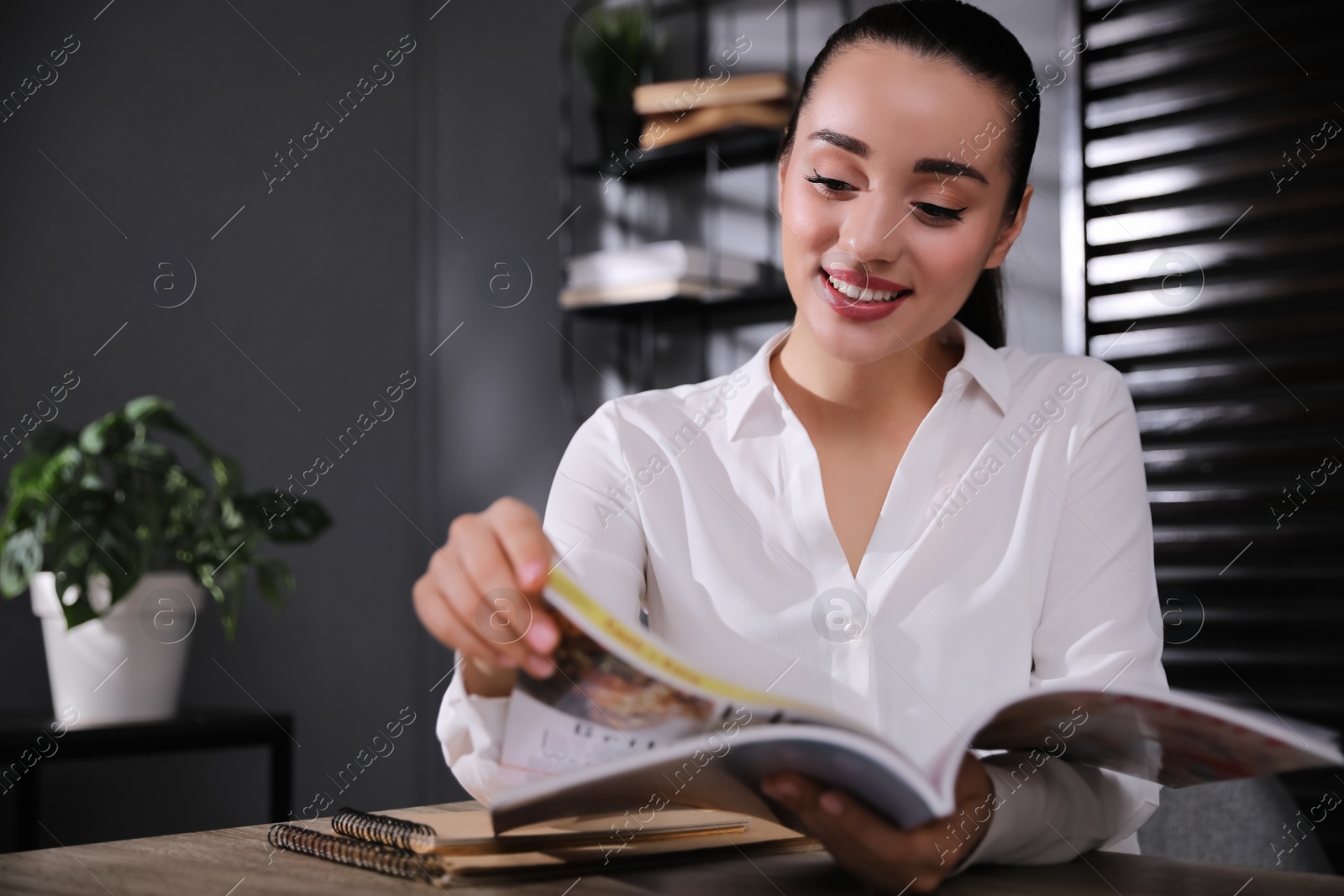 Photo of Happy woman reading magazine at workplace in office