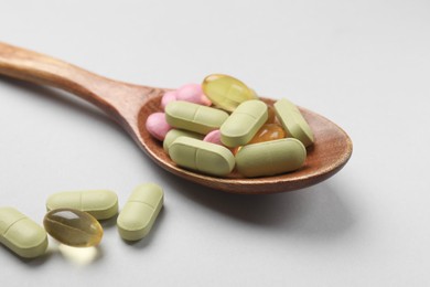 Photo of Different vitamin pills in wooden spoon on light grey background, closeup