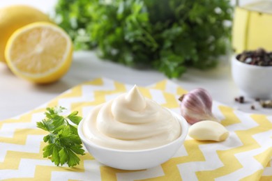 Tasty mayonnaise sauce in bowl, parsley and garlic on table, closeup