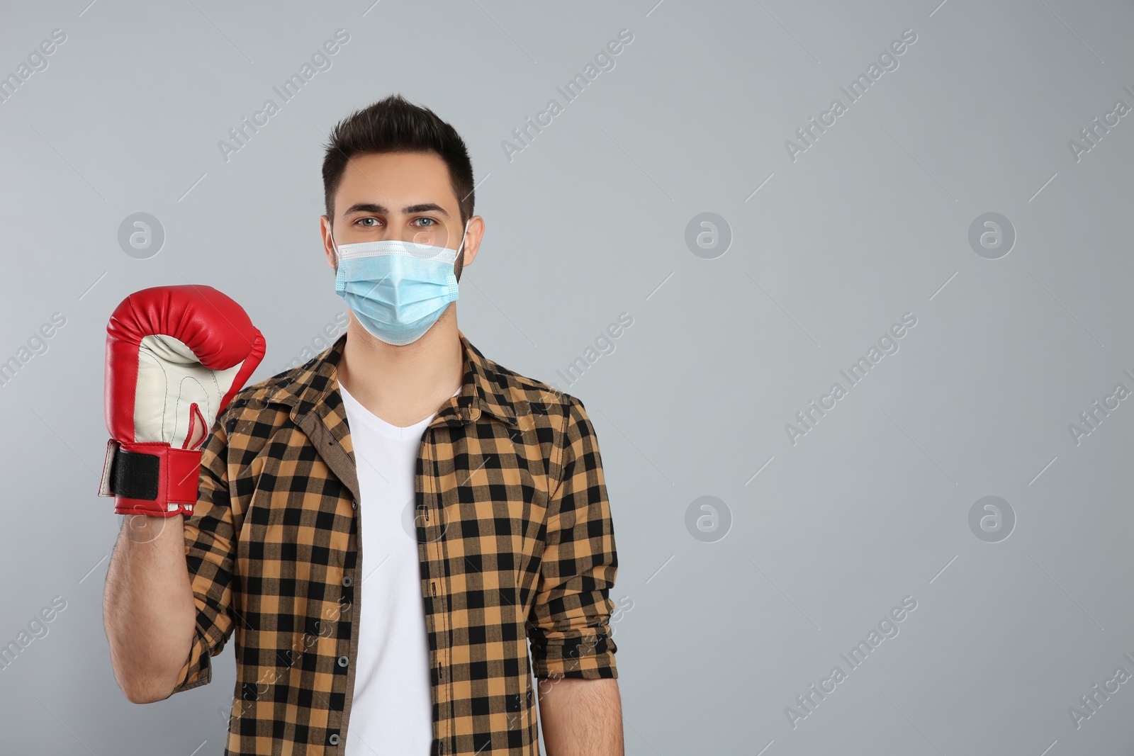 Photo of Man with protective mask and boxing gloves on light grey background, space for text. Strong immunity concept