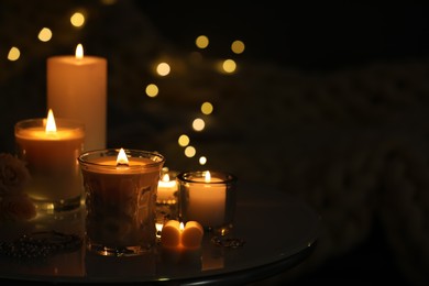 Photo of Beautiful burning candles on table in darkness. Space for text