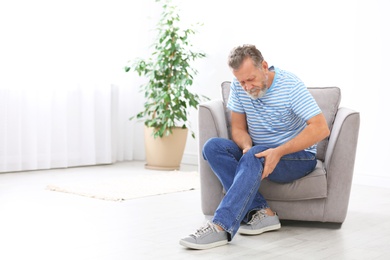Photo of Senior man suffering from knee pain in living room. Space for text