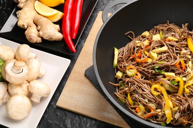 Photo of Stir-fry. Tasty noodles with vegetables, meat in wok and ingredients on dark textured table