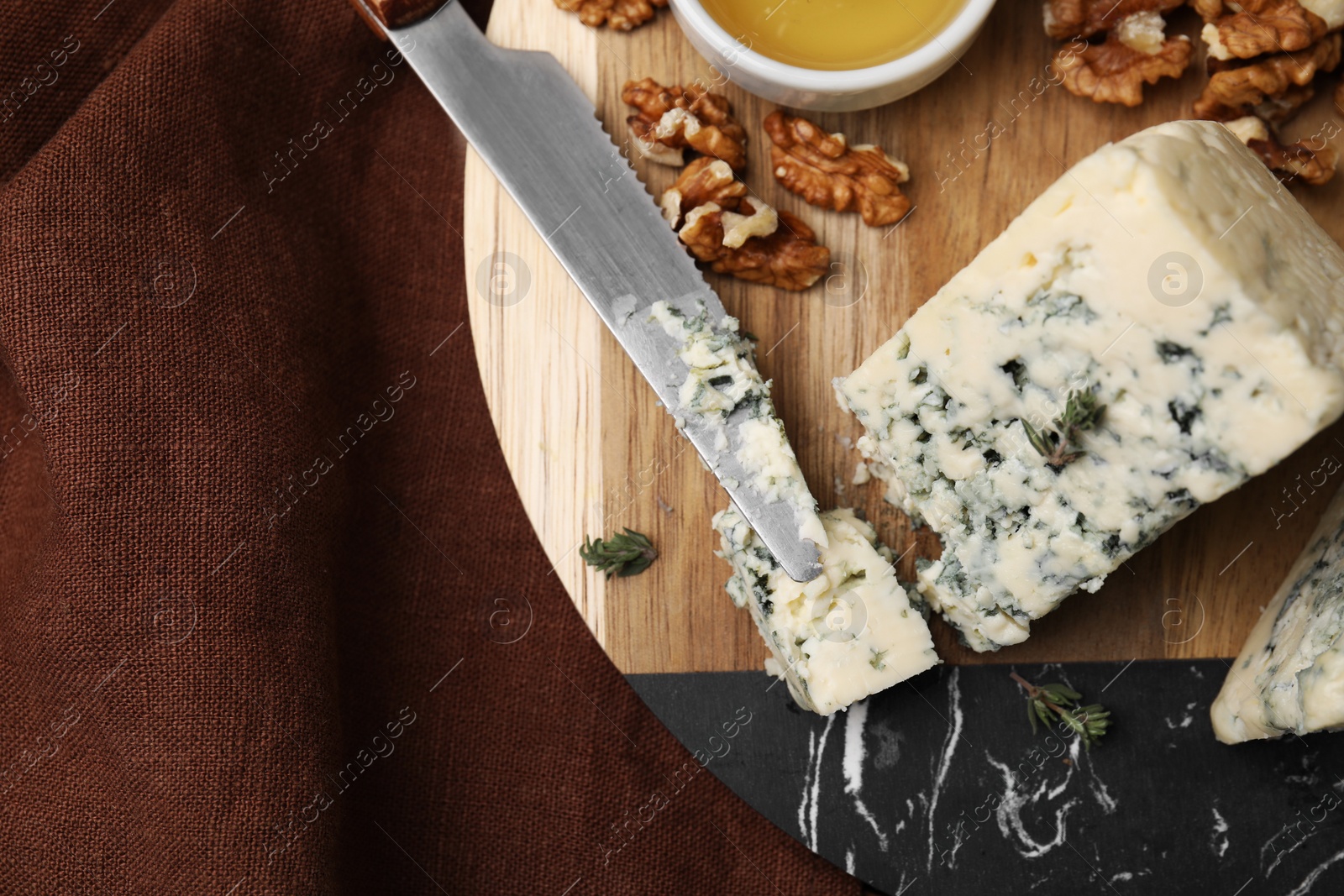 Photo of Tasty blue cheese with thyme, honey and walnuts on wooden board, top view