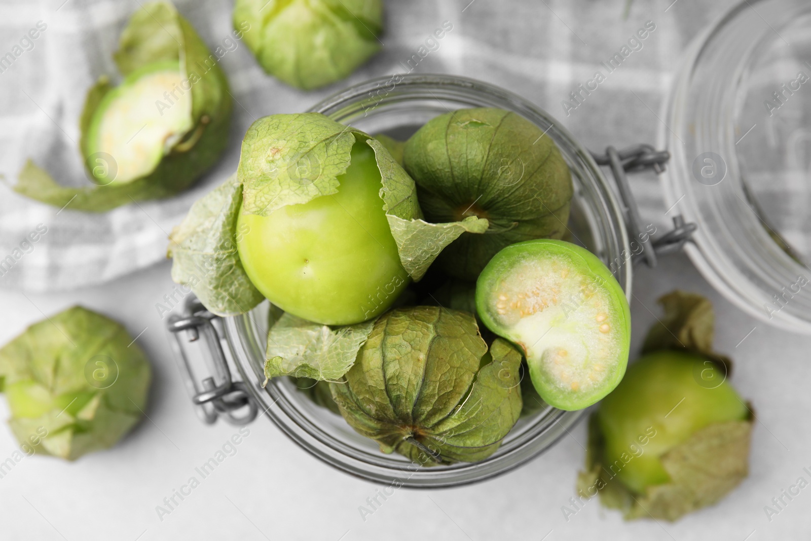 Photo of Fresh green tomatillos with husk in glass jar on light table, flat lay