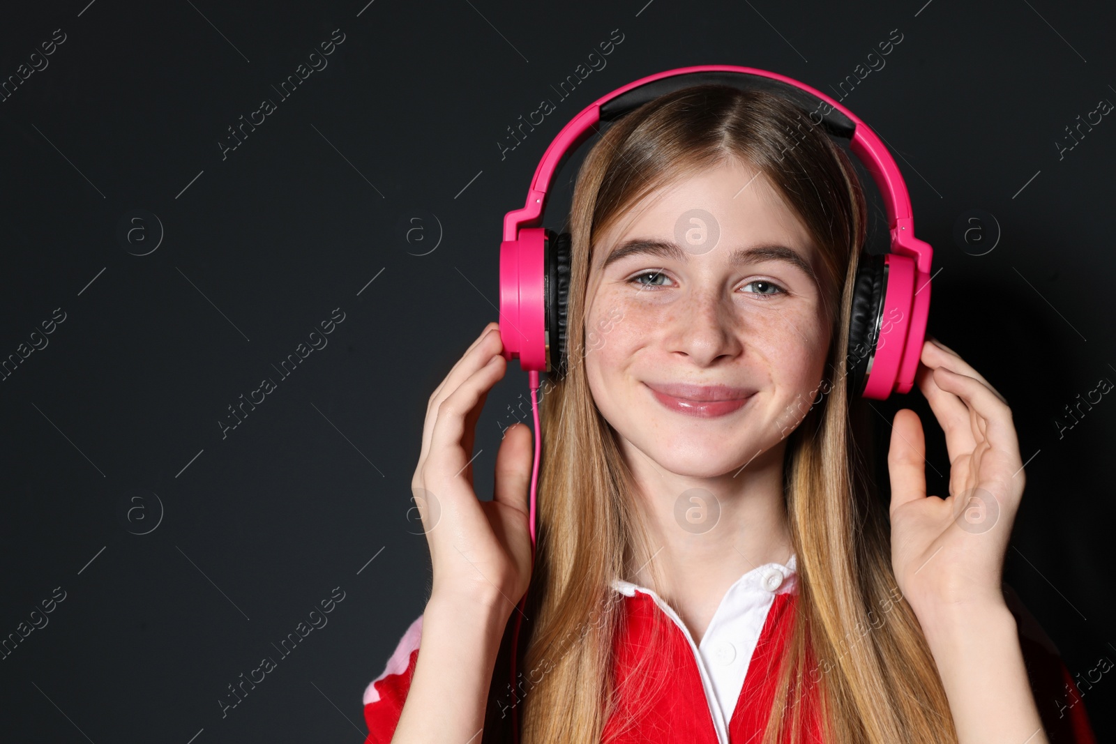 Photo of Teenage girl enjoying music in headphones on black background. Space for text