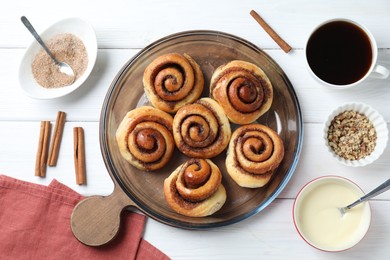 Tasty cinnamon rolls and ingredients on white wooden table, flat lay