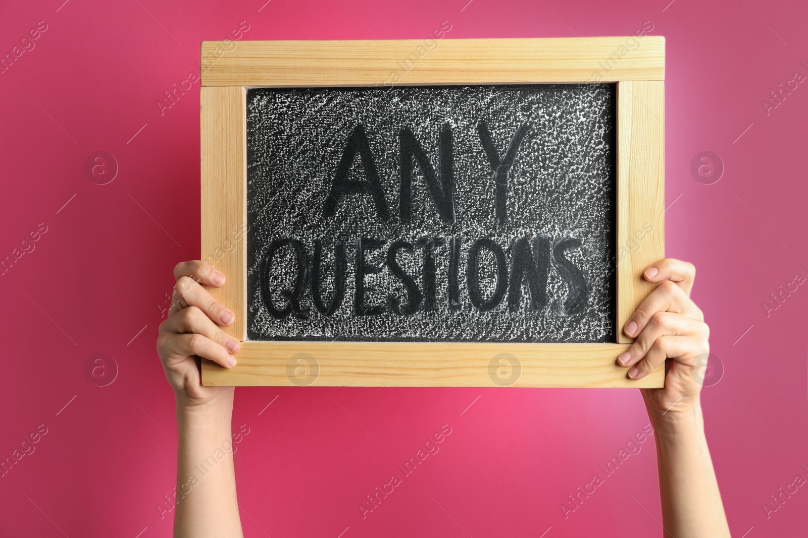Photo of Woman holding blackboard with phrase ANY QUESTIONS on pink background, closeup