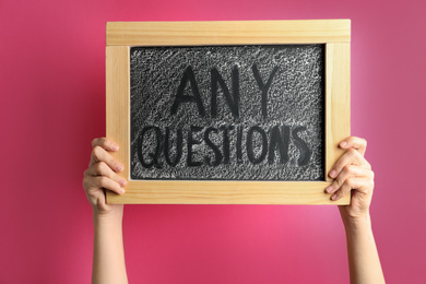 Woman holding blackboard with phrase ANY QUESTIONS on pink background, closeup