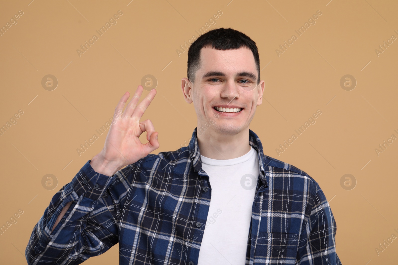 Photo of Handsome young man with clean teeth smiling and showing OK gesture on beige background