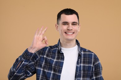 Photo of Handsome young man with clean teeth smiling and showing OK gesture on beige background