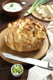 Photo of Freshly baked bread with tofu cheese, green onions, sauce and knife on wooden table