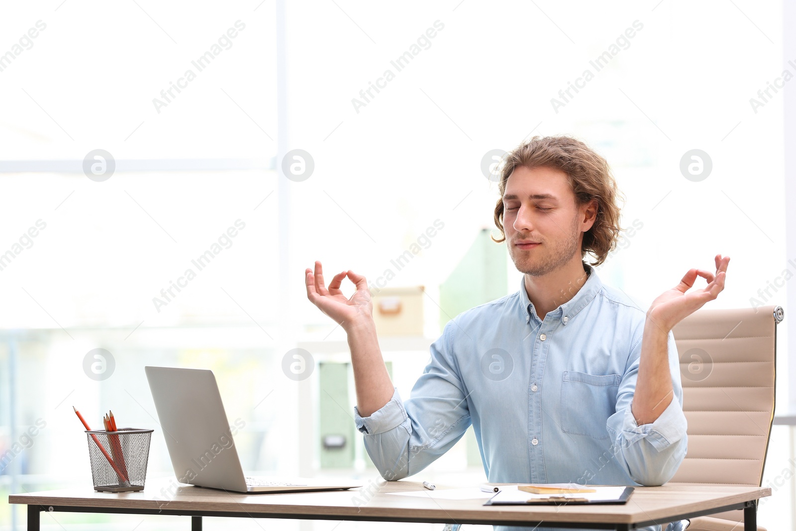 Photo of Young businessman meditating at table in office during break. Zen yoga