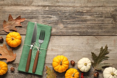 Photo of Cutlery, napkin and autumn decoration on wooden background, flat lay with space for text. Table setting