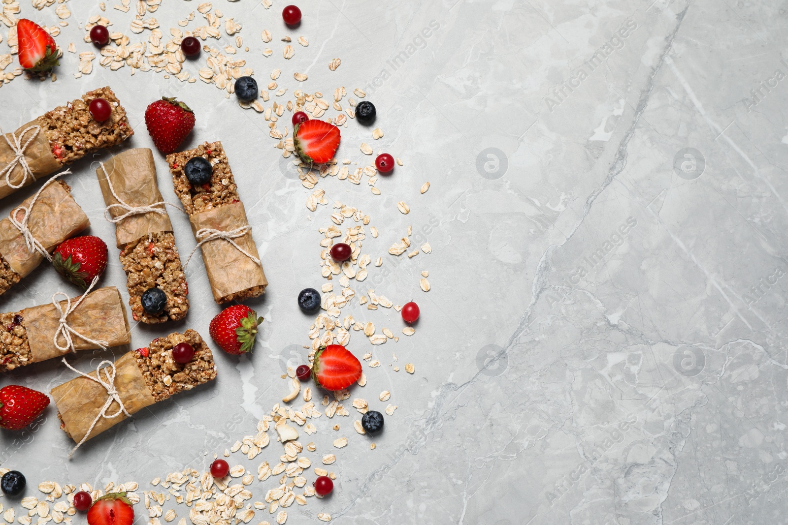 Photo of Tasty granola bars and ingredients on light grey marble table, flat lay. Space for text