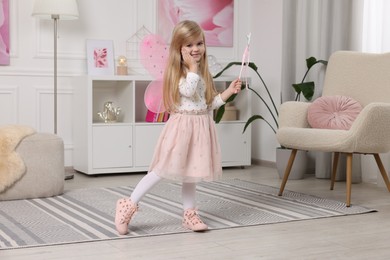 Cute little girl in fairy costume with pink wings and magic wand at home