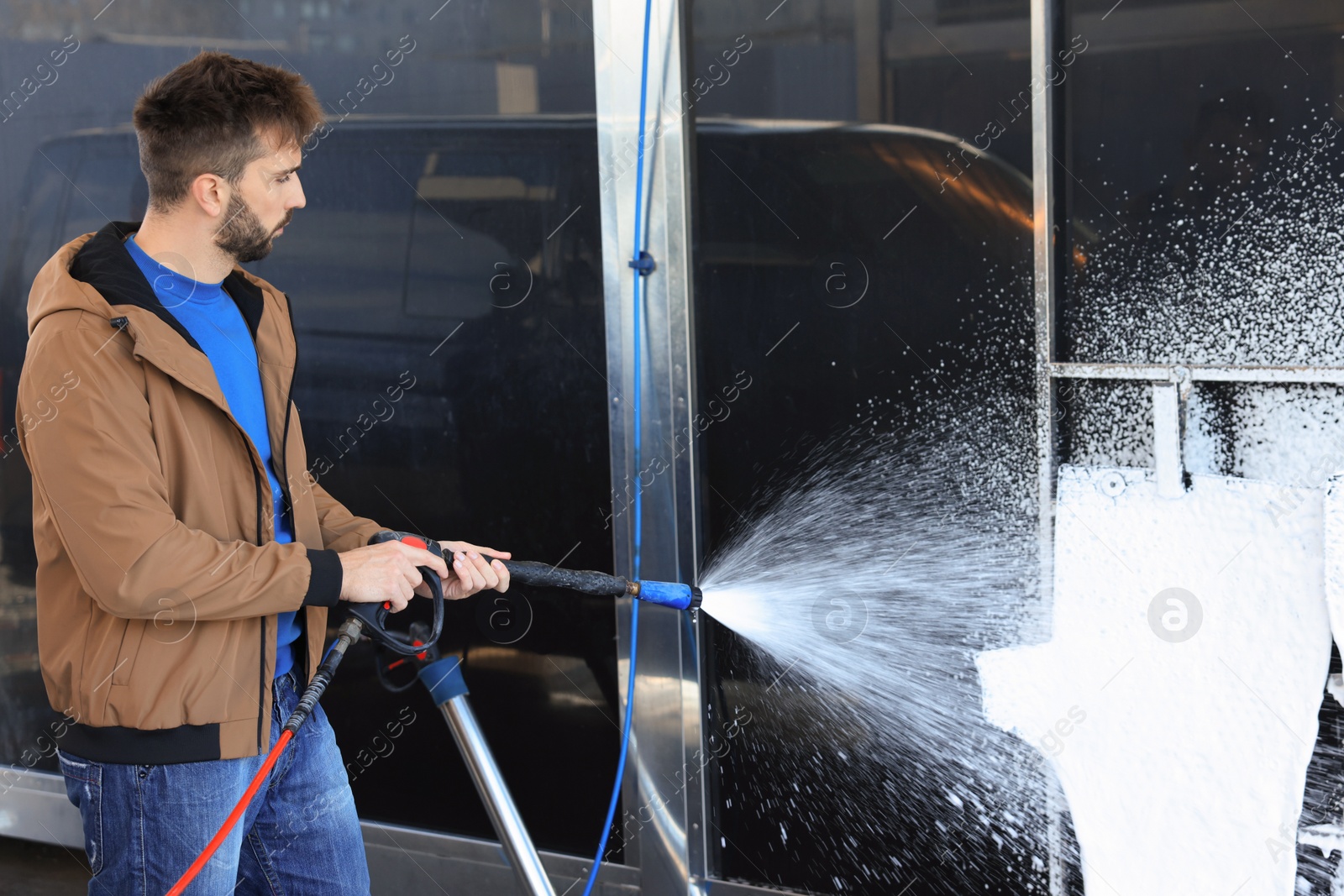 Photo of Man cleaning auto mats with high pressure foam jet at self-service car wash