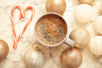 Flat lay composition with cup of hot winter drink and Christmas balls on marble table. Cozy season