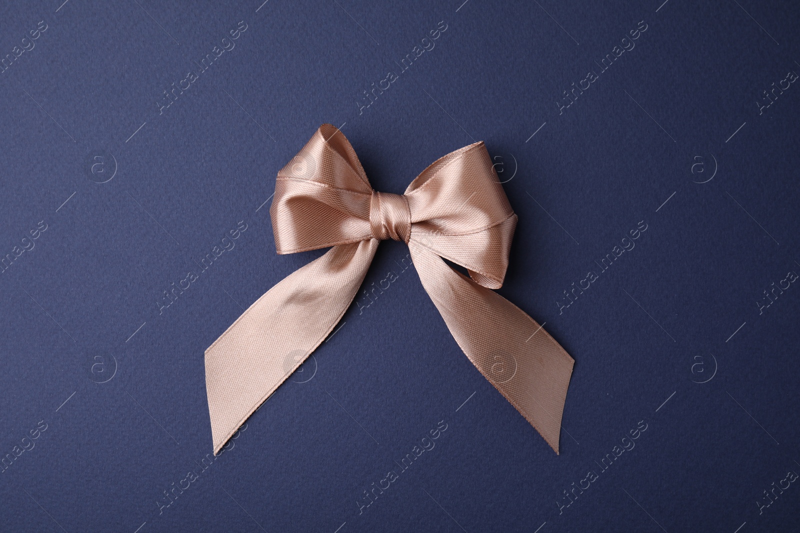 Photo of Beige satin ribbon bow on blue background, top view