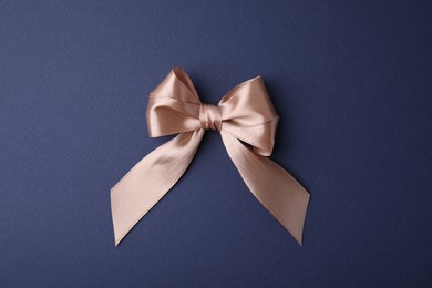 Beige satin ribbon bow on blue background, top view