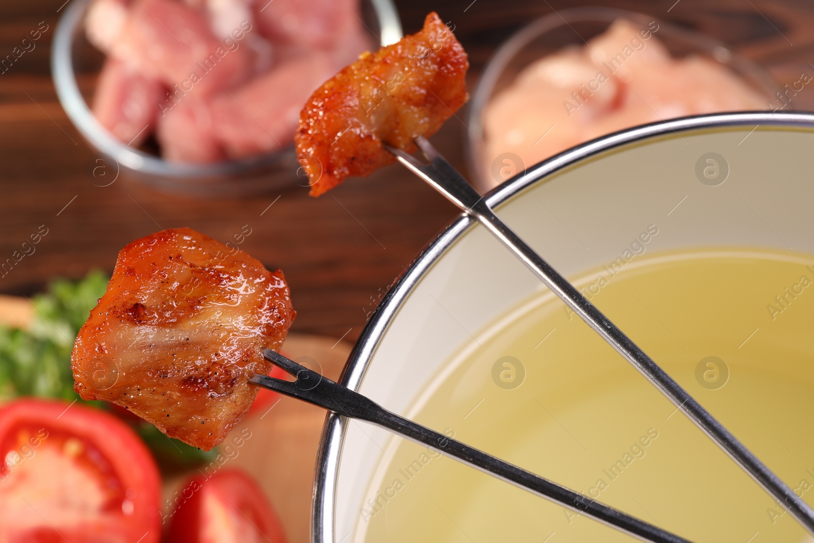 Photo of Fondue pot, forks with fried meat pieces and other products on wooden table, closeup