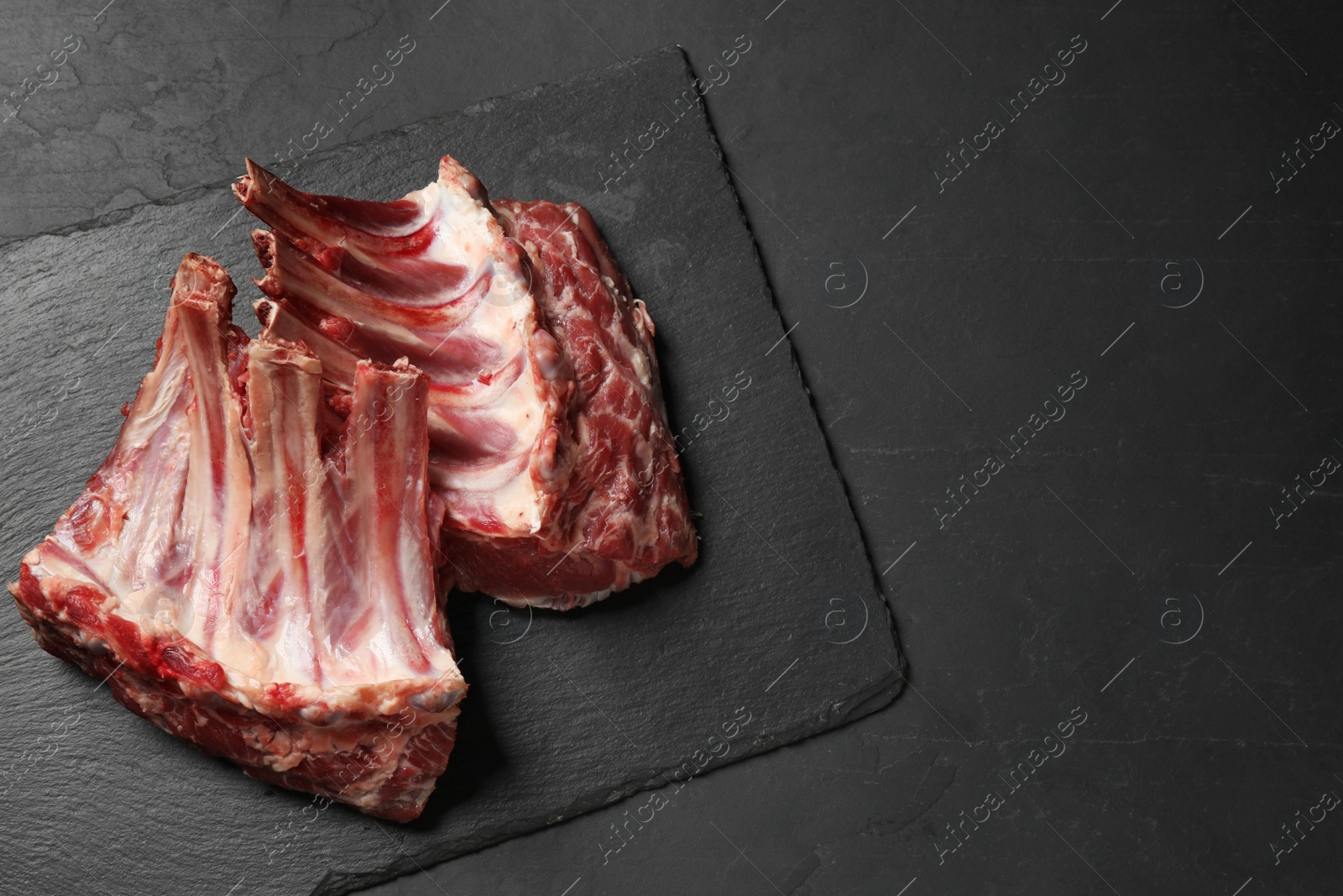 Photo of Raw ribs on black table, top view. Space for text